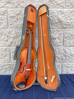 Open violin case showing violin inside with bow attached to the right side and a wooden shoulder rest inside the lid.