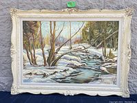 Front view of the oil painting in ornate cream-colored frame showing winter creek scene.