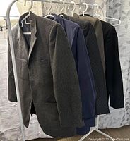 Six men's suit coats and pants hanging on hangers, showing different colors and patterns.