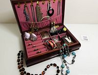 Open view of the vintage wooden jewelry box with multiple pieces of vintage jewelry including necklaces, rings, earrings, bracelets displayed inside compartments and the hanging section.