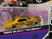 Front side view of unopened yellow Buick Riviera diecast model with black flame decals in original packaging.
