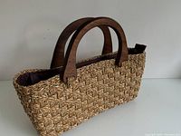 View of the woven handbag showing the natural fiber weaving with wooden handles.