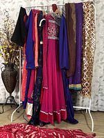 Photo of the full rack showing all eight traditional dresses hanging on a white metal garment rack, featuring various colors and embellishments.