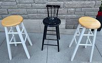 Three stools placed side by side: two white wooden barstools with natural wood seats and one black antique wooden stool with backrest, showing used condition.