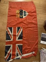 1967 Canadian Red Ensign flag with Union Jack and three green maple leaves shield laid flat on wooden floor.