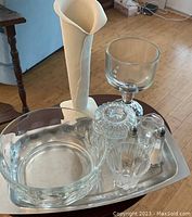 Photo showing the stainless steel serving tray holding multiple glass items and a white clay lily vase, arranged on a wooden floor.