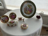 Lot overview showing large Limoges plate, two smaller plates, lidded containers, harp miniature in frame, rose figurine on round table with window light