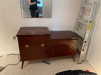 Side view of mid-century wooden blanket chest showing two drawers and cabinet door with brass hardware, placed on carpeted floor.