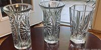 Photo showing three heavy clear glass vases on a table, two identical cylindrical vases with starburst pattern and one smaller hexagonal vase