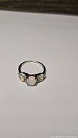 Full view of the ring showing three opal stones set in a silver band with white gold plating.
