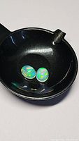 Close-up photo of the pair of oval cabochon Ethiopian opals with vibrant play of color sitting in a small black container.