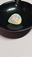 Photo showing polished untreated Ethiopian opal gemstone with vivid play-of-color, placed in a black round container against a white background.