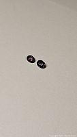 Two oval shaped deep purple sapphires placed on a light surface, showing their color and cut from a top angle.