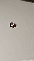 Angled view of the deep orange oval cut Tanzanian zircon gemstone on a flat surface showing color and facets.