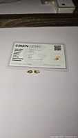 Photo of two pear cut natural golden citrine gemstones alongside a certification card showing details such as material, color, clarity, dimensions, and certification number.