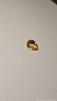 Close-up image of a pear-shaped golden citrine gemstone on a white background, showing good clarity and faceting details.