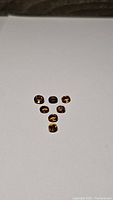 Seven faceted gemstones in deep golden orange whiskey color on white background