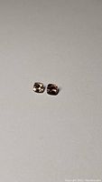 Two small cushion cut tourmaline gemstones on plain background, showing pinkish-orange and orange hues.