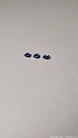 Three pear-shaped Tanzanite gemstones shown side by side on a neutral background emphasizing size and color