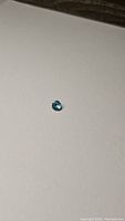 Close up photo of a small round brilliant-cut bright lagoon ocean blue gemstone resting on light surface.