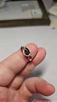 Close-up front view of pear-shaped purple pink rhodolite garnet ring held on finger showing gemstone and accent stones