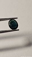Close up photo of blue oval sapphire held by tweezers showing color and cut