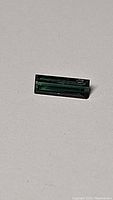 Close-up photo of single baguette cut tourmaline gemstone showing deep blue-green color and rectangular shape