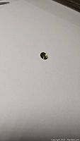 Close-up photo of a small bright deep yellow tourmaline oval cut gemstone on white paper, showing the stone's color and cut details.