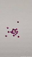 Several small round cut pink-purple-red rubies scattered on a white background, showing clarity and color.