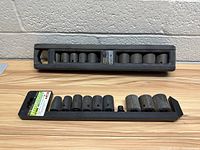 Two sets of metal impact sockets arranged in plastic trays on a wooden surface.