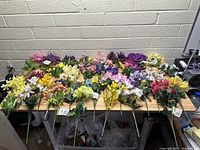 Top-down photo showing an extensive assortment of artificial flower bunches laid out on a table with multiple colors and types.