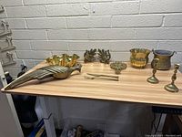 Wide shot of all brass items on table showing peacock figurine, bowls, candle holders, and decorative pieces