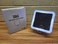 Photo showing front view of JiBen LED square mirror with LED light border illuminated and original box next to it.