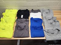 Top down view of folded work shirts in various colors including neon yellow, black, gray, white and blue.