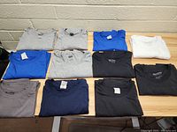 Full view of all 11 folded Gildan shirts arranged on table in various colors as described in the lot.