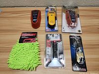 Top-down view of the lot items on a wood-patterned surface, showing all included items: three stud finders, one green microfiber wash glove, one flashlight, one coupler lock with keys.