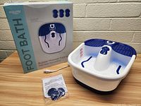 Photo showing boxed product with foot bath and accessories on a wooden table against a brick wall.