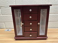 Front view of wooden jewelry box showing 5 drawers with metal knobs, flanked by 2 glass door side compartments.