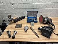 Photo showing assorted power and hand tools on a wooden surface against a white brick wall.
