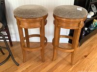 Pair of matching wooden barstools with beige patterned upholstered seats shown together.