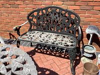 Wrought iron bench shown in sunlight, displaying overall structure and design with floral patterns on the back and seat.