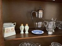 Middle shelf of china cabinet showing salt and pepper shakers, sugar bowl, creamer, crystal bowl, glass coffee pot with metal lid and handle, Wedgwood dish