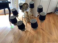 Overall view of brass chandelier showing eight arms with black shades.