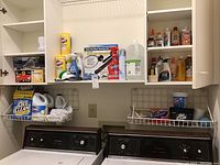 Wide shot of laundry area with cabinets open displaying bottles of cleaning supplies including Clorox, OxiClean, Shout, Brasso, Resolve, Downy, and insect repellent.