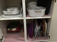 Open cabinet with white Corningware casseroles on top shelf, assorted cutting boards stored vertically on bottom shelf.