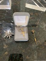Front view of the three pins including 14kt gold cross pendant in box, snowflake pin and gold filled BellSouth pin on dark surface.