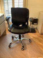 Front view of black faux leather and mesh desk chair with metal base and caster wheels, showing padded seat and armrests