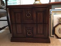 Close-up view of front panel showing two drawers with brass circular pull handles and paneled wood grain finish.