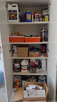 Top and middle shelves of cabinet containing assorted paint cans, caulk tubes, mineral spirits, gloves, and boxes of painting supplies