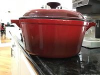Side view of red Le Creuset cast iron enamel Dutch oven with lid on black countertop.